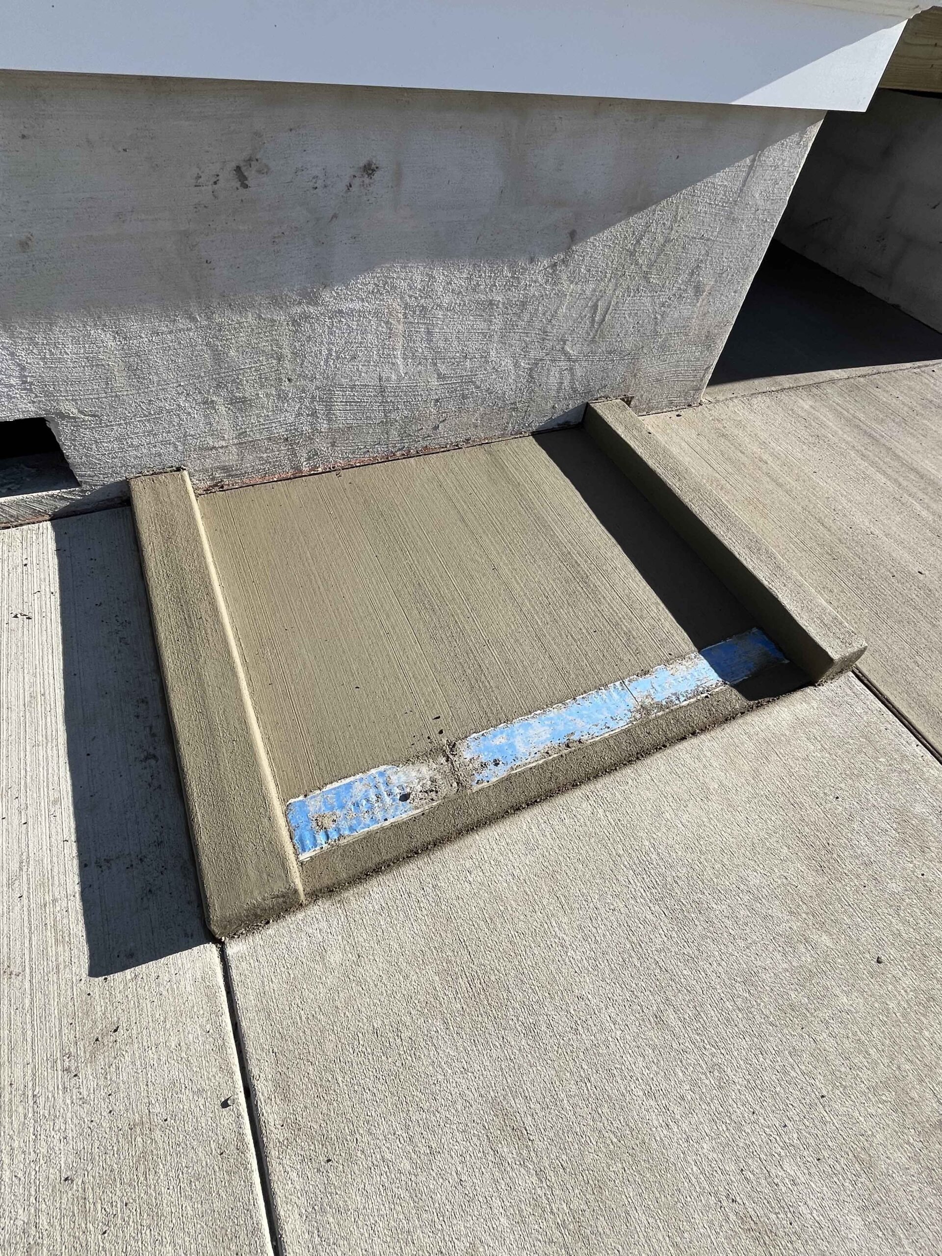 A close-up of a freshly resurfaced concrete entry step showing a smooth troweled mortar finish with a blue tape edge guide still in place, flanked by existing concrete slabs.