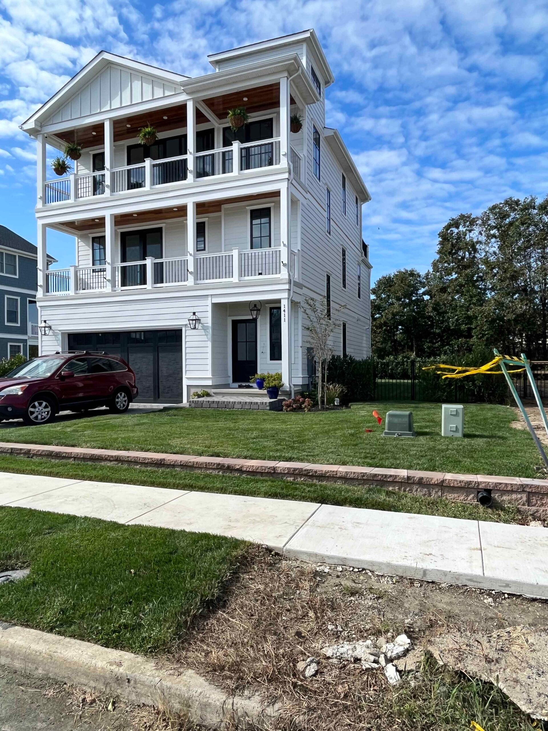 Freshly installed sod covers the front yard of a three-story white coastal-style home with a concrete driveway and front walkway. The lawn edges are clean-cut, and small ornamental plantings in blue pots flank the front entry.