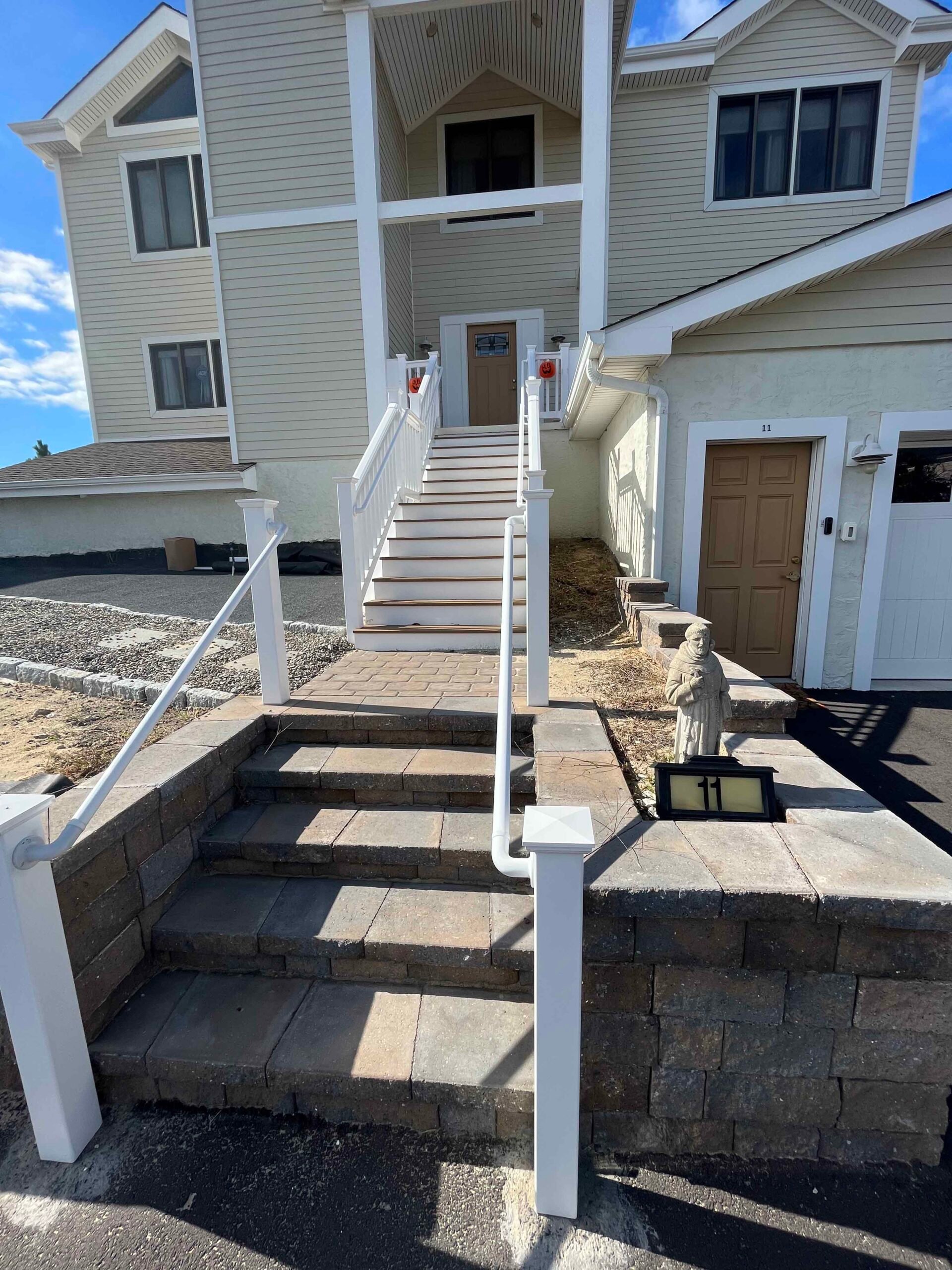 Newly installed concrete paver steps with white aluminum railings lead up to a residential entry, flanked by a stacked concrete block retaining wall with a paver cap; surrounding ground is bare with brown mulch, indicating a recently completed hardscape in